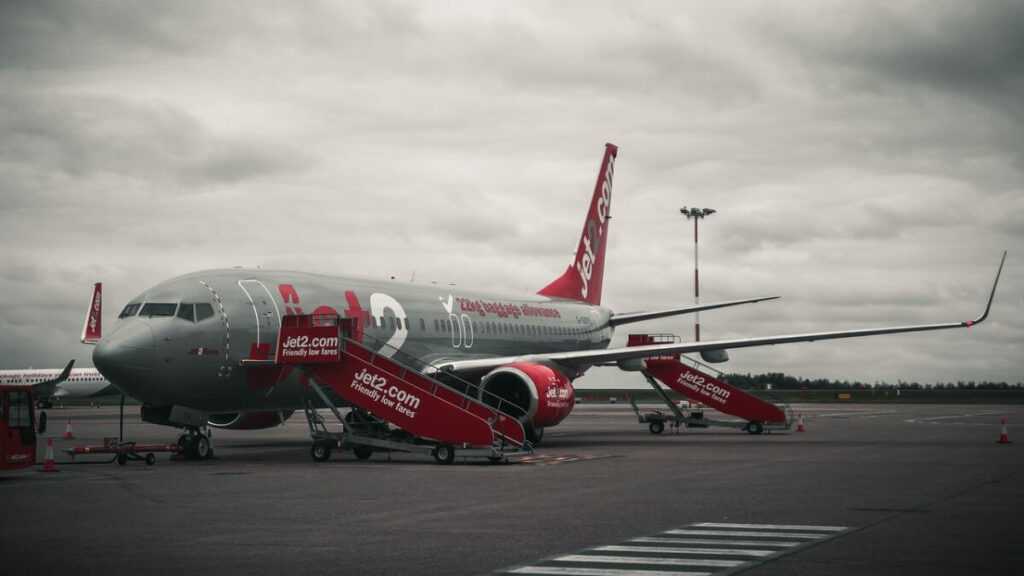 Avião vermelho e cinza parado em um aeroporto sendo preparado para embarque de passageiros