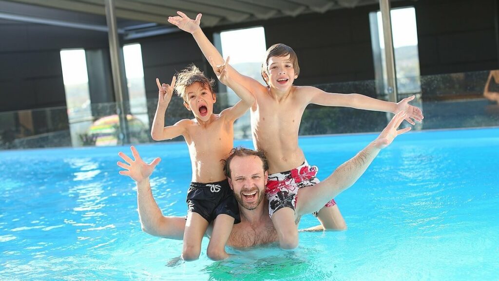 Homem com dois meninos em seu ombro em uma piscina grande