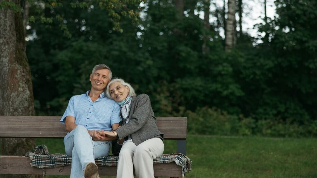 Casal de idosos, sentados em um banco de madeira, em meio a floresta de um parque