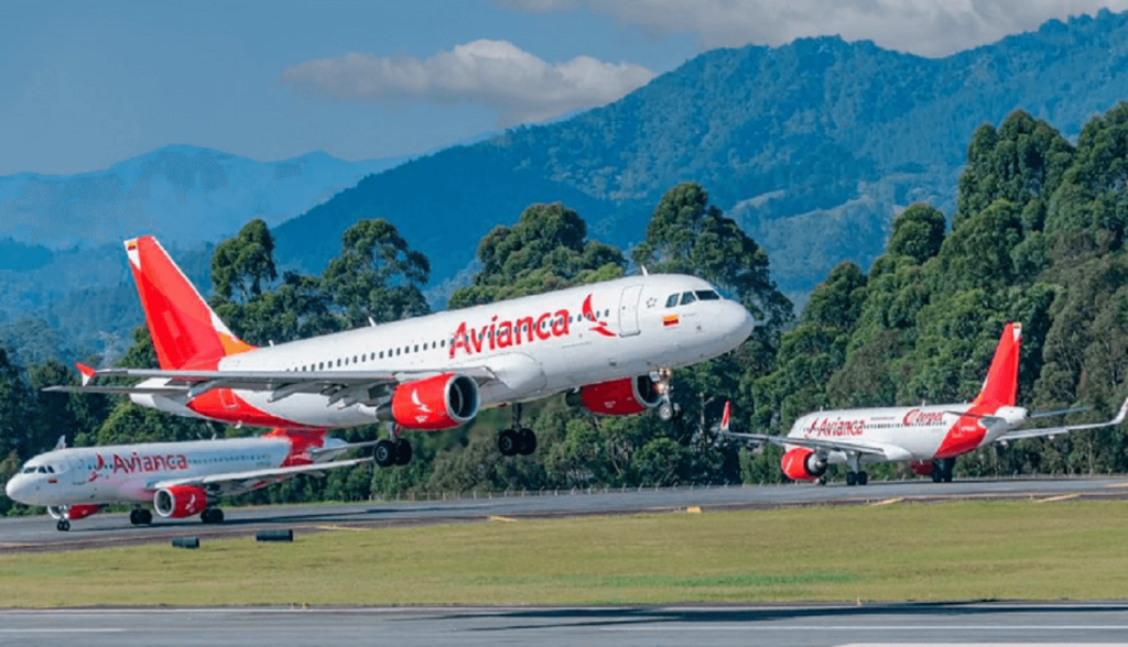 Aviões branco com nome e logomarca da Avianca em vermelho pousando e decolando em um aeroporto com montanhas ao fundo