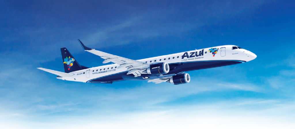 Avião da Azul nas cores branco com azul forte e logomarca da empresa voando em céu com poucas nuvens