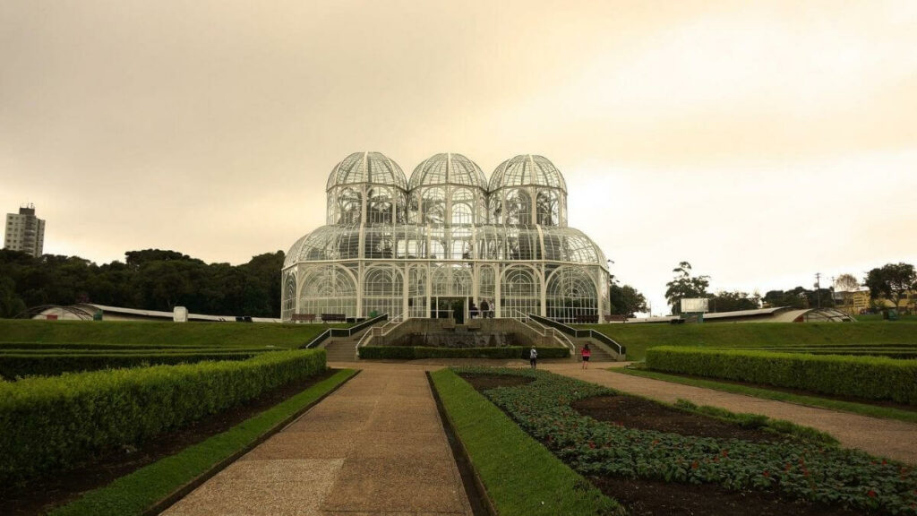 Jardim Botânico de Curitiba. Grande jardim com flores e uma estrutura metalica