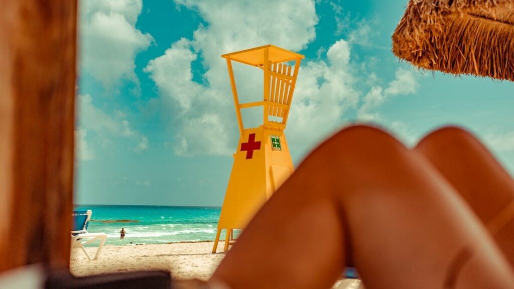 Pessoa sentada na sombra, com um posto de salva vidas ao fundo