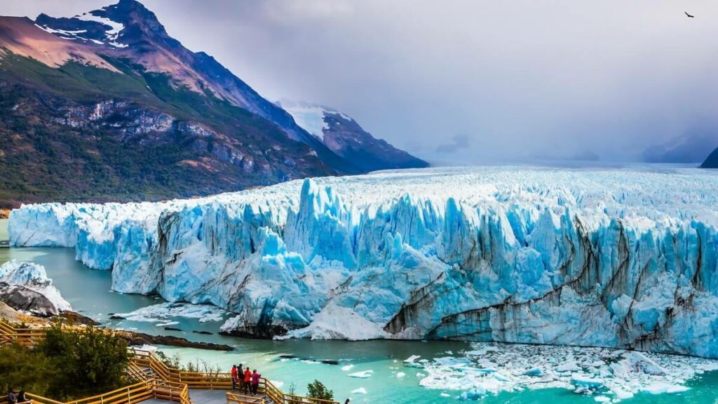 A imagem apresenta as geleiras da região de El Calafate com grandes montanhas ao fundo.