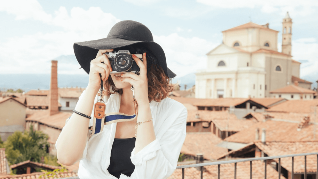 mulher com roupa branca e chapéu preto segurando uma câmera para tirar uma foto