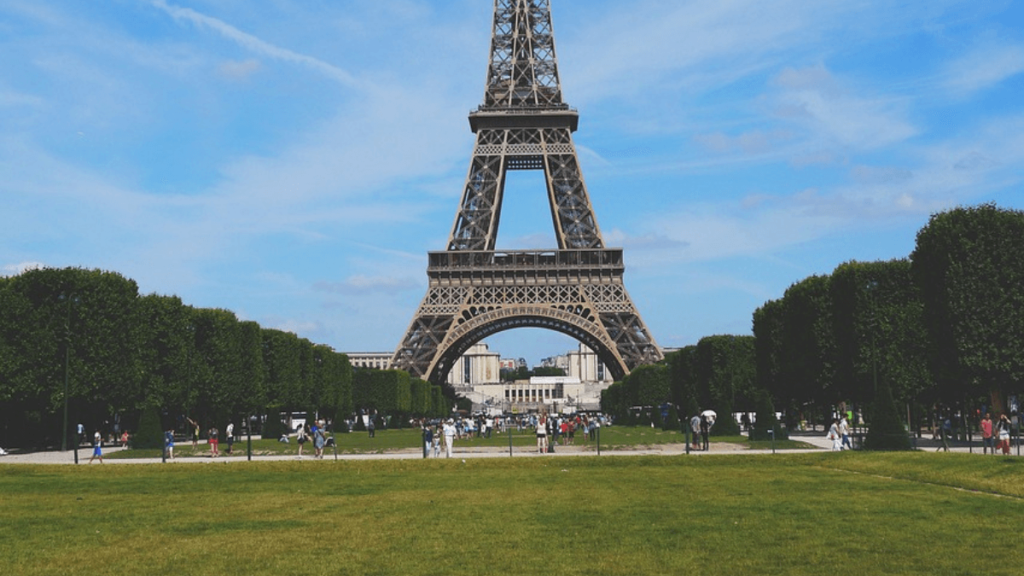 Gramado verde com arvores ao redor em frente a Torre Eiffel.