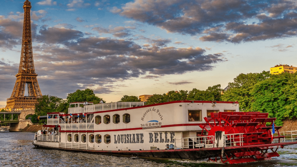 Barco branco e vermelho navegando pelo Rio Sena com uma visão privilegiada da Torre Eiffel durante o dia.