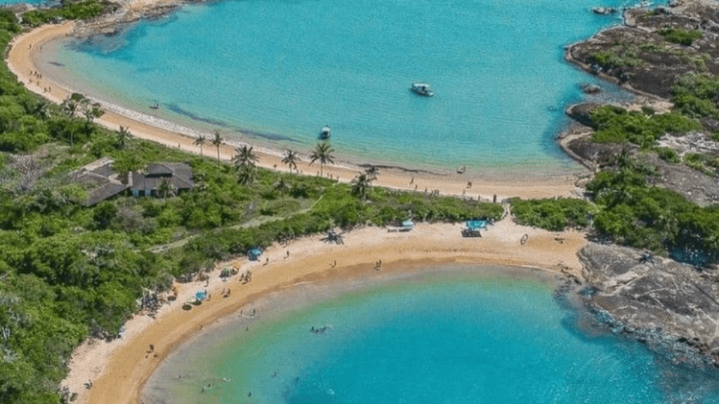 praia de guarapari com muita vegetação, areia branca e mar limpo