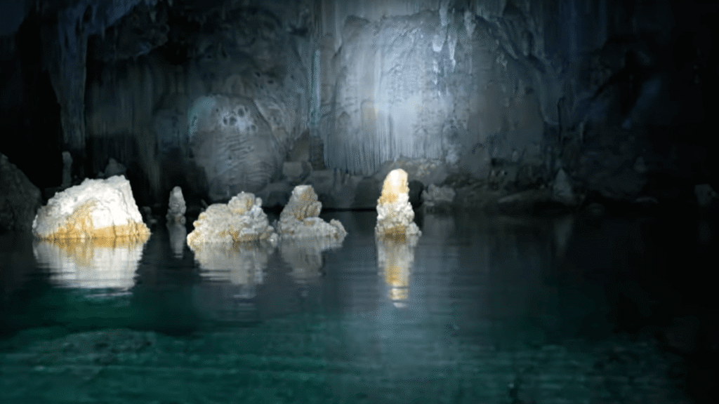 Caverna escuro com uma lanterna iluminando pedras no meio da água.
