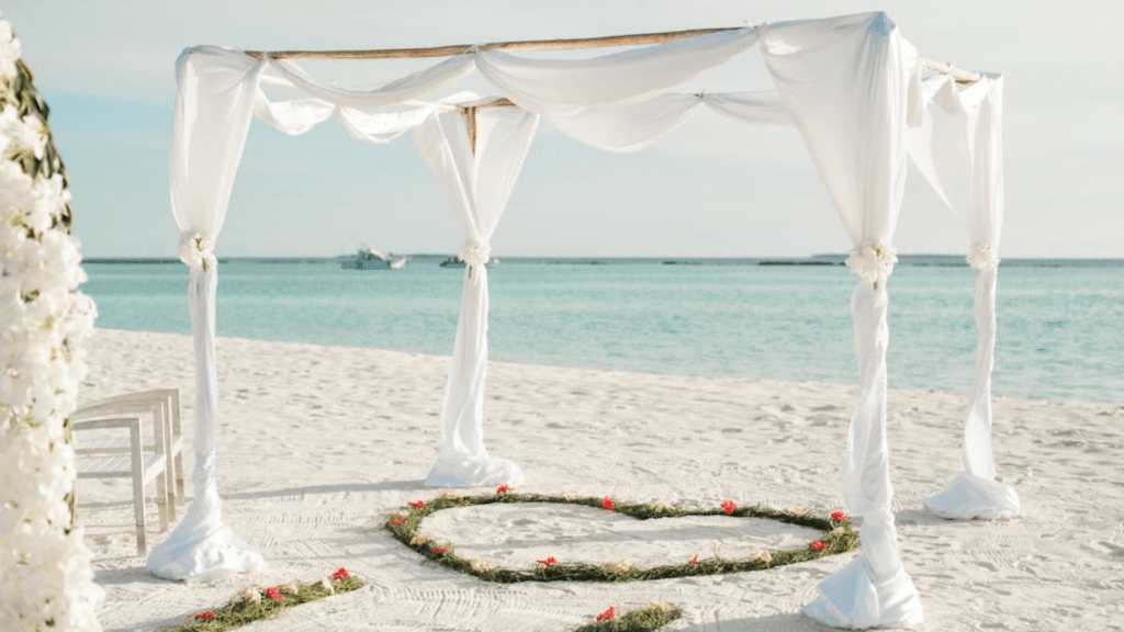Casamento na praia com uma tenda branca e um desenho de coração na areia.