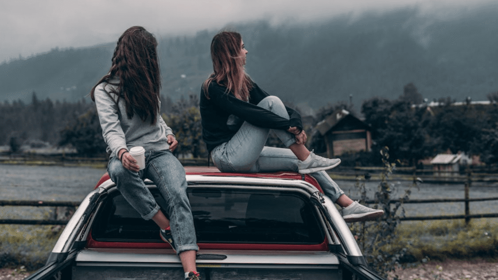 Duas mulheres sentadas em cima de uma caminhonete vermelha com um lago no fundo.