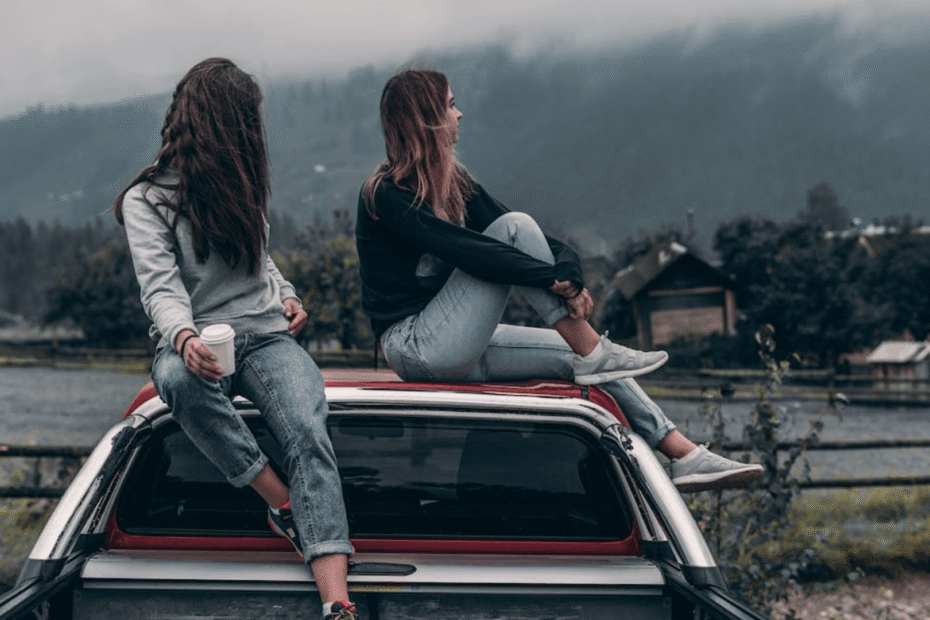 Duas mulheres sentadas em cima de uma caminhonete vermelha com um lago no fundo.