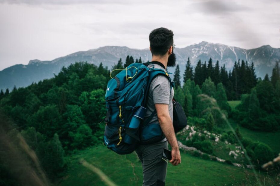 Homem de mochila em cima de uma montanha com uma vista para a floresta.